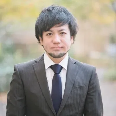 ビジネススーツを着たアジア系の男性がカメラをまっすぐ見ている上半身の肖像画です。