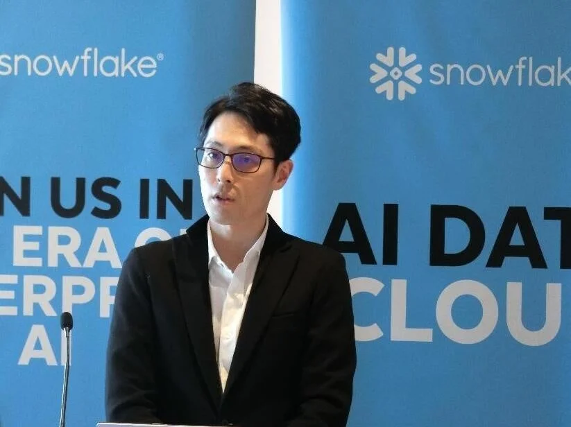 SnowflakeのロゴとAI DATA CLOUDの文字が映る背景でプレゼンテーションを行う男性