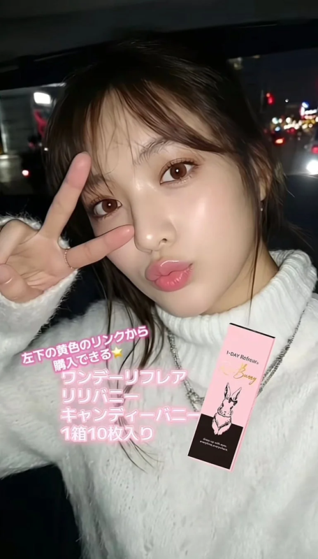 若い女性がピースサインをしており、光沢のある唇と白いふわふわのセーターを着用