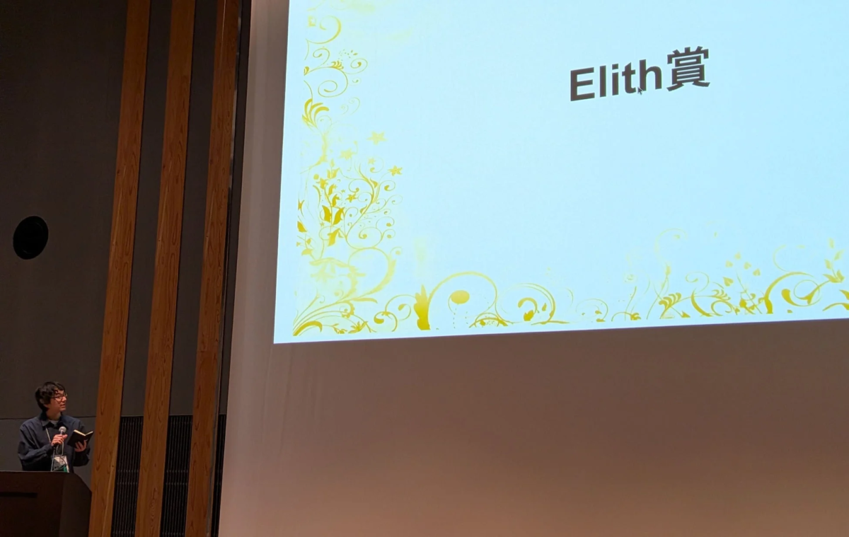 講演台に立つ男性がマイクを持ち、背後のスクリーンには「Elith賞」という文字が表示されています