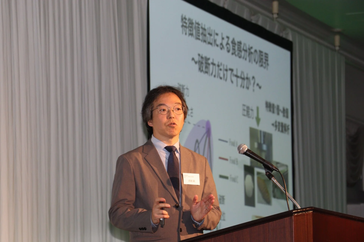 プレゼンテーション中の男性が「食感分析」に関するスライドを背景に話している