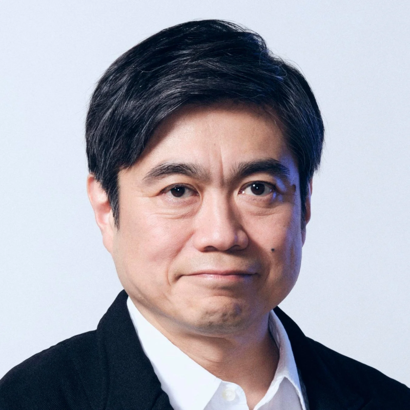 白い背景の前で、黒いジャケットと白いシャツを着用したアジア系の中年男性のポートレートです。真面目で落ち着いた表情をしており、プロフェッショナルな印象を与えます。