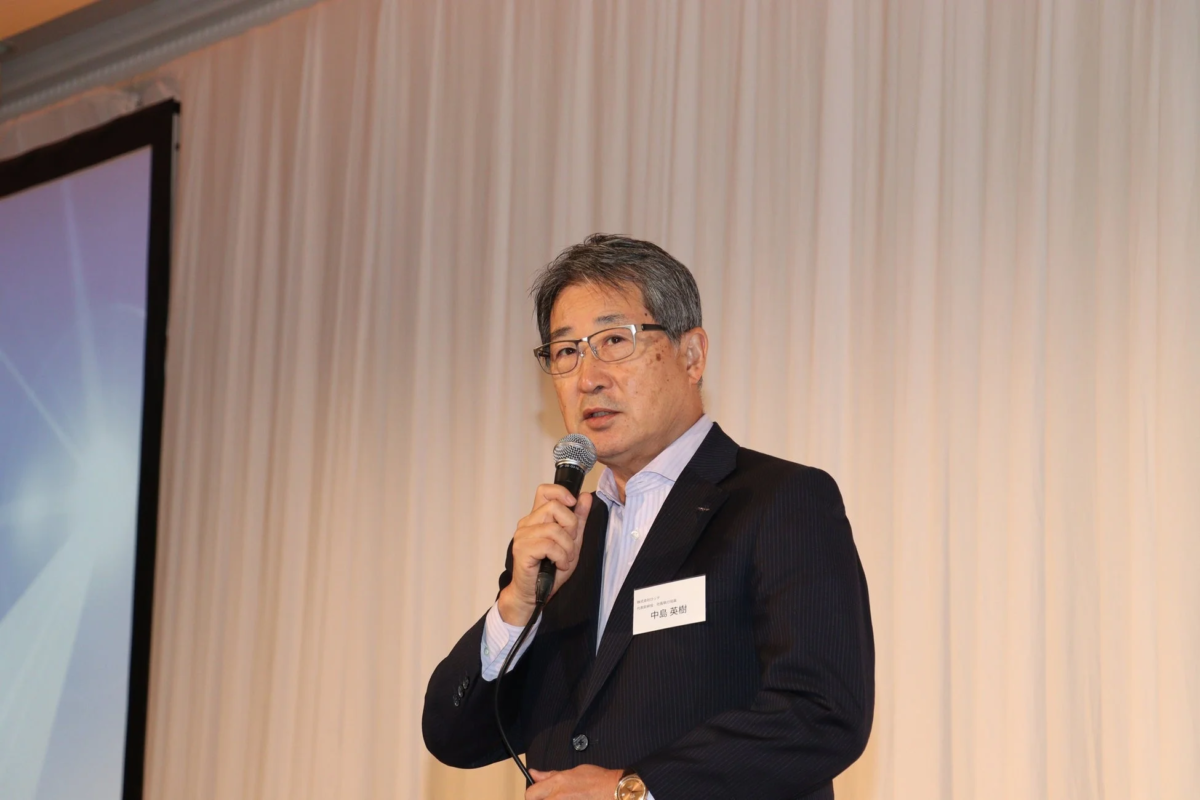 スーツ姿の男性がマイクを持ってスピーチしている