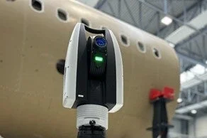 航空機の胴体らしき背景に、緑色のランプが点灯した高精度な3Dスキャン装置が設置されている様子を捉えた画像です。産業用途での精密測定や検査に使われる最新技術を示唆しています。