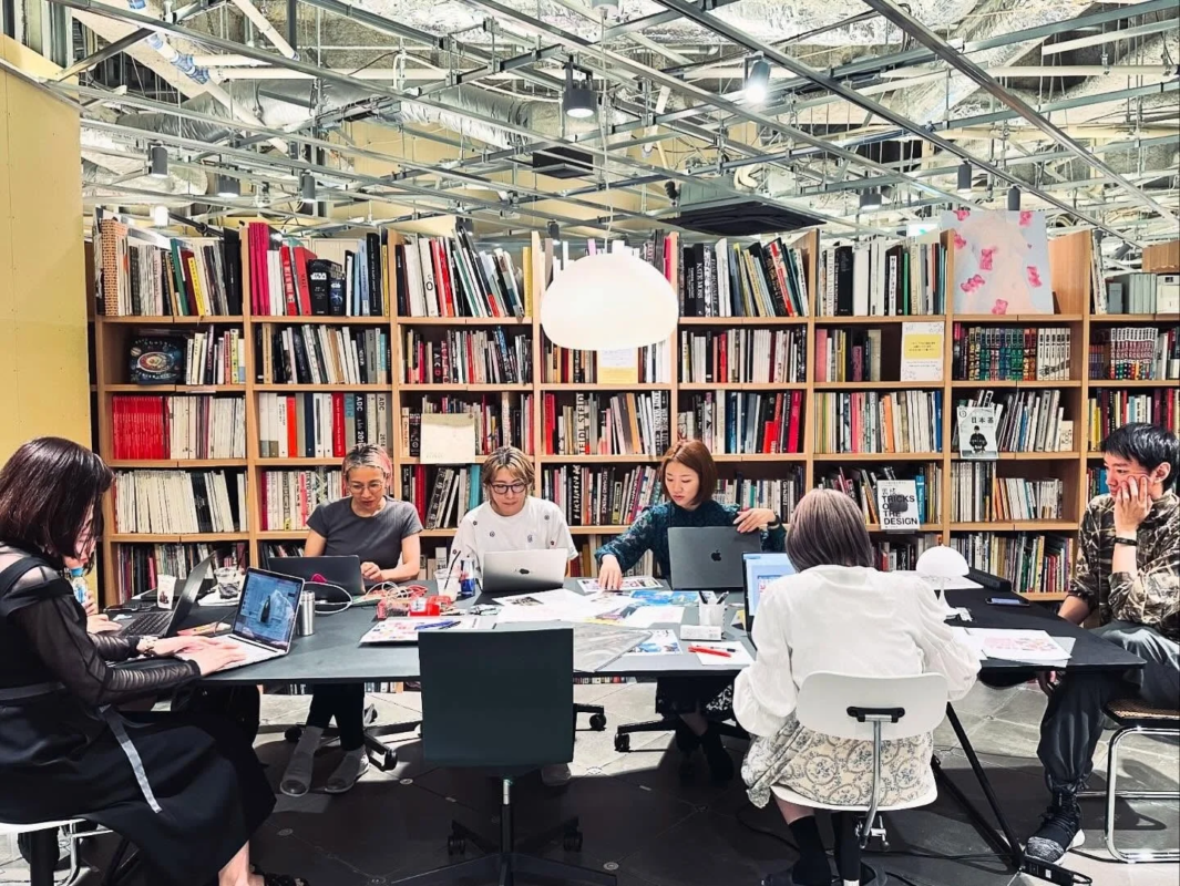 モダンなオフィス空間で、複数の人々が大きなテーブルを囲んでノートパソコンを使い作業している様子