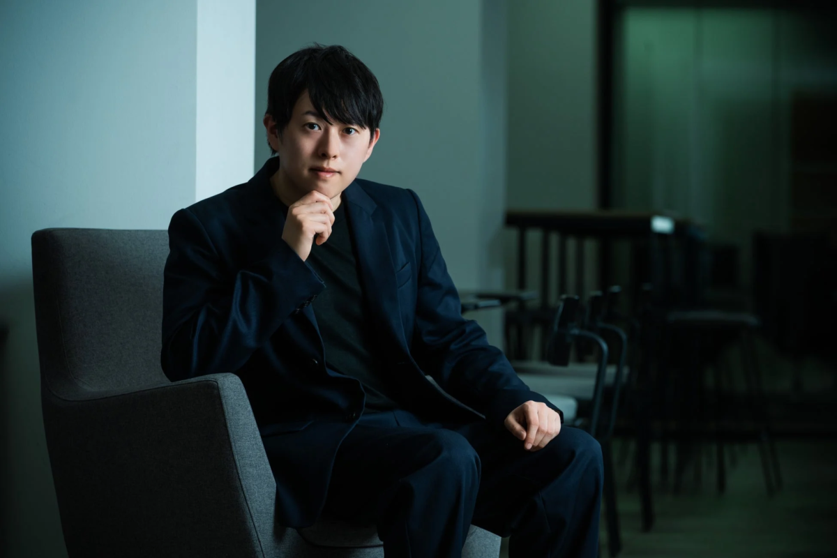 暗い色のスーツを着て考えるポーズをとるElithの人物