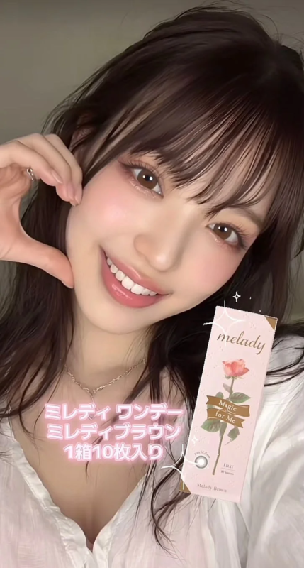 笑顔の女性がカラコン「ミレディワンデー ミレディブラウン」のパッケージを持ち、頬に手を当てたポーズをとっている