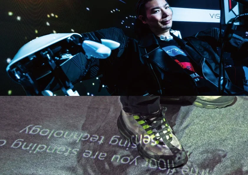 ロボットアームを装着し笑顔を見せる男性と、足元に「you are standing on the floor technology」と投影された床が印象的です。先進技術の展示会やイベントの様子を捉えており、未来的な雰囲気が漂います。