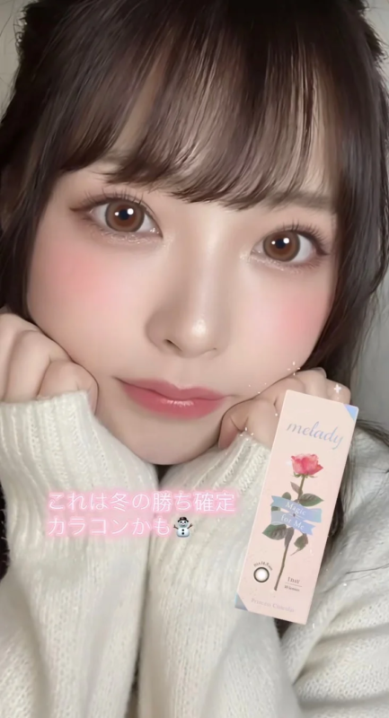 白いニットを着た女性が、meladyのカラーコンタクトレンズの箱を持ってカメラを見つめている