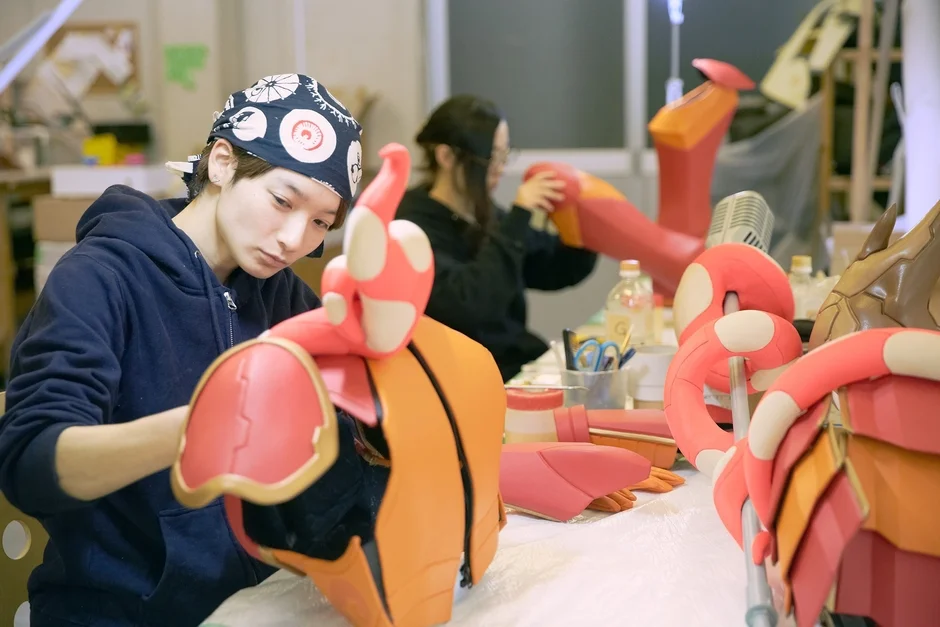 赤とオレンジ色の大きな造形物を丁寧に制作している
