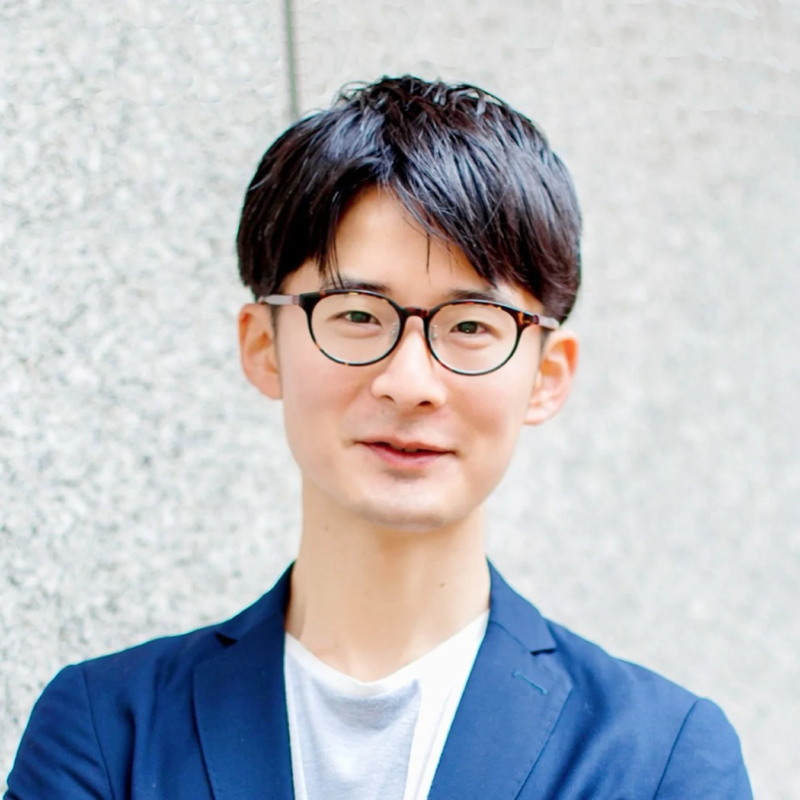 眼鏡をかけた若いアジア人男性が紺色のジャケットを着て微笑んでいるポートレート