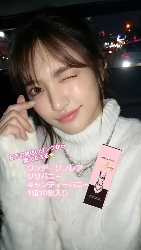 白いタートルネックを着た女性がウィンクし、ピンク色の「ワンデーリフレア キャンディーバニー」のカラコンの箱を持っている