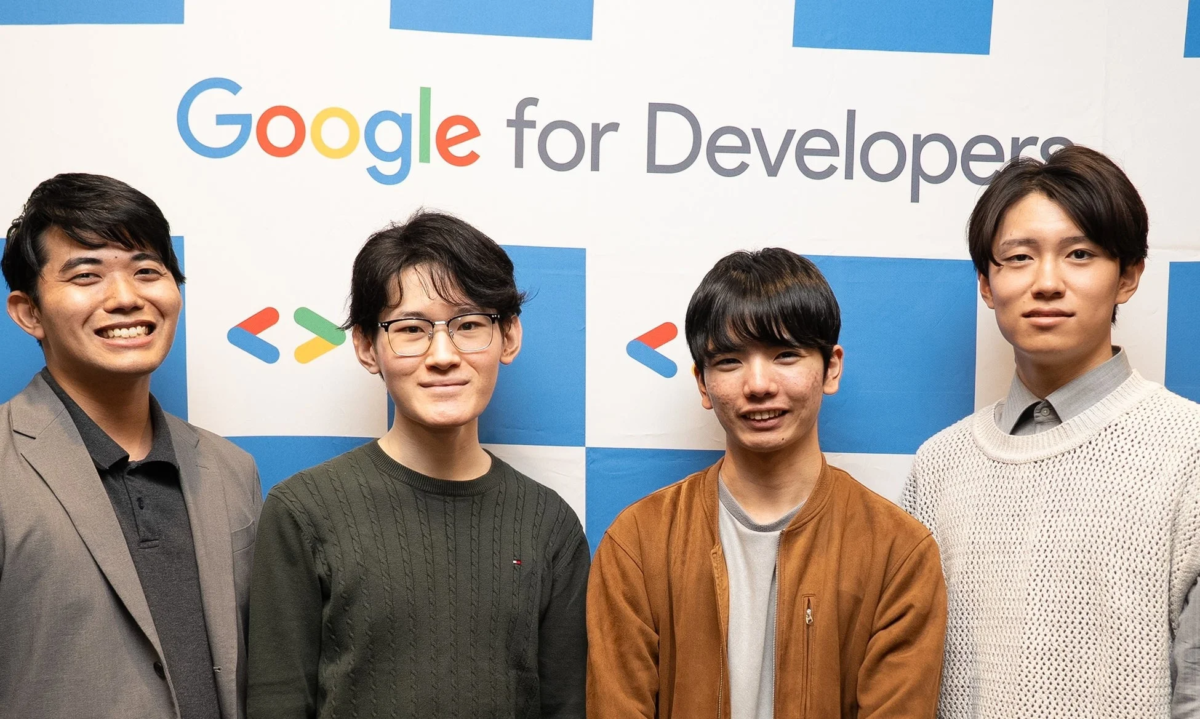 Google for Developersのロゴが描かれた背景の前で、4人の若い男性が並んで笑顔を見せている集合写真です。