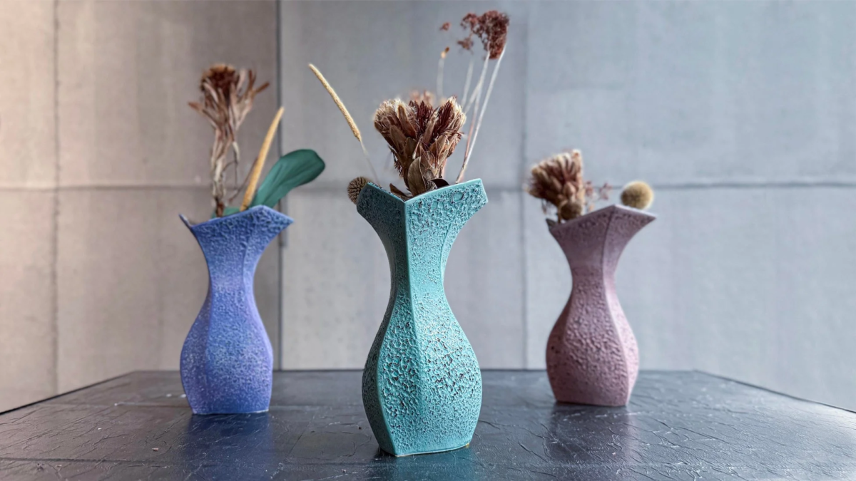 暗い質感のテーブルに、青、水色、ピンクの3つの異なる色の花瓶が並べられ、それぞれにドライフラワーが生けられています。花瓶の独特な形状と質感が特徴的で、モダンなインテリア装飾として映える一枚です。
