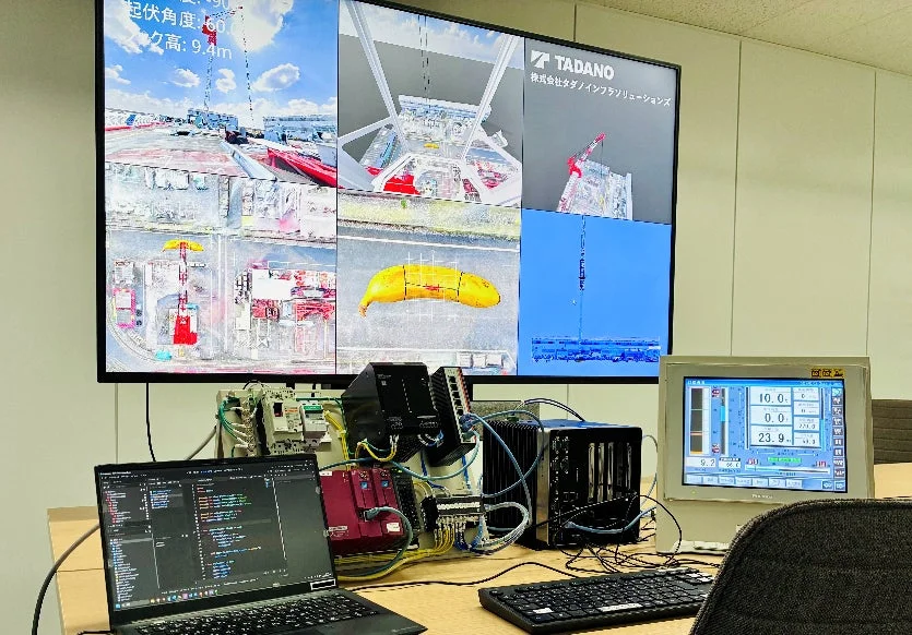 クレーンのシミュレーション画面が表示されたディスプレイと開発中のオフィス風景