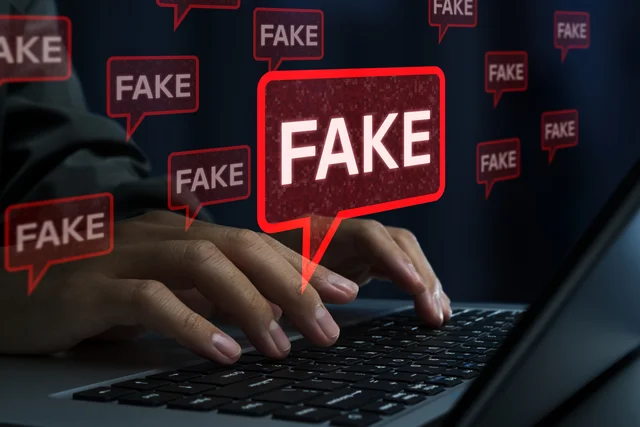 ノートパソコンを操作する人物の手元が写されており、その上には「FAKE」と書かれた吹き出しが複数浮かんでいます。これはフェイクニュースや誤情報の拡散、オンライン詐欺などを暗示しています。
