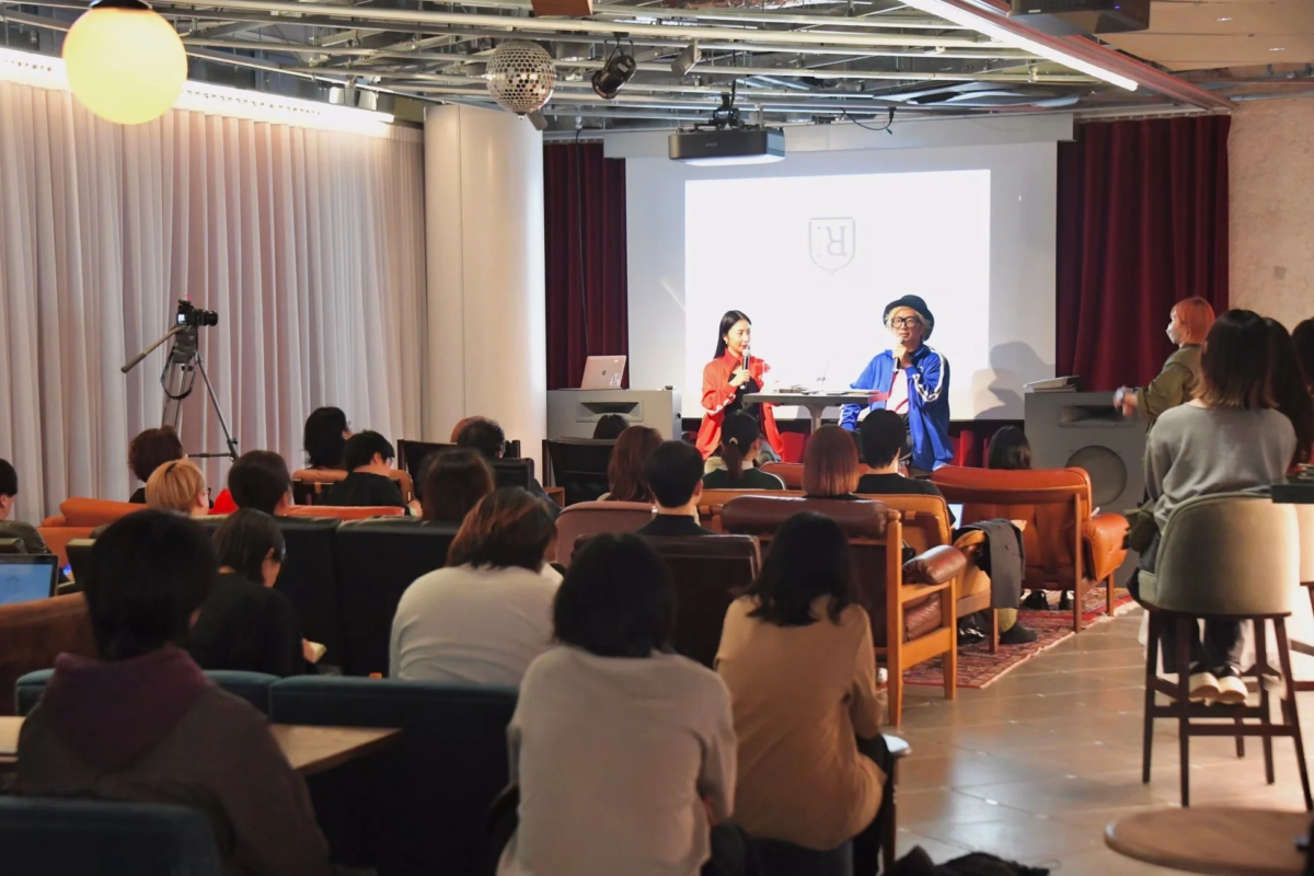 現代的な雰囲気の会場で、二人の登壇者がマイクを持って聴衆に向けて話している様子