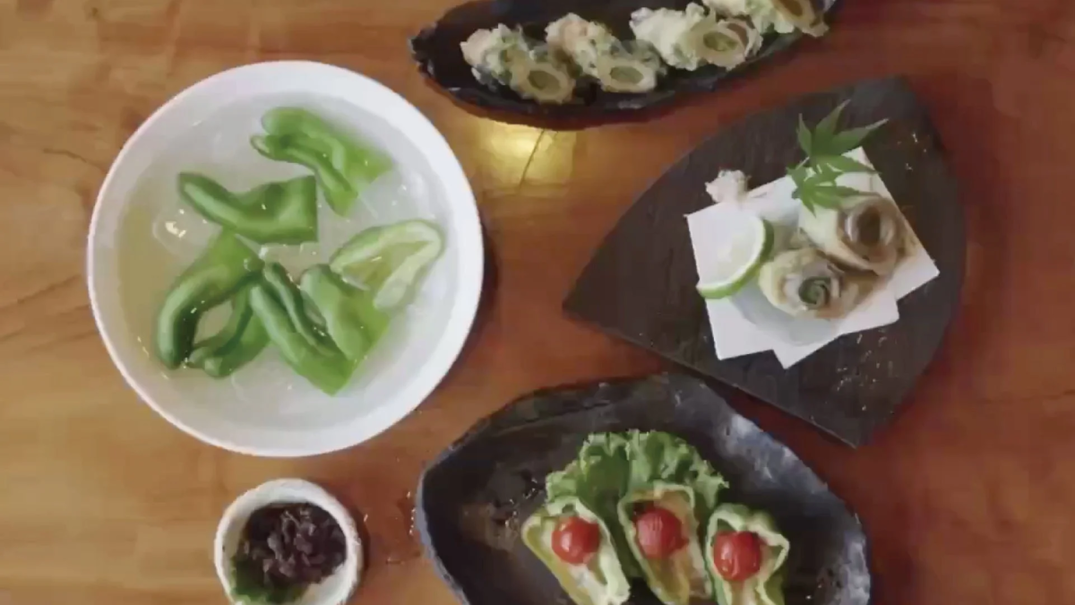 食卓に並べられた複数の和風料理。水に浸かったピーマン、揚げ物、ピーマンとミニトマトの盛り付けなど、色とりどりの野菜を使った料理が特徴的です。