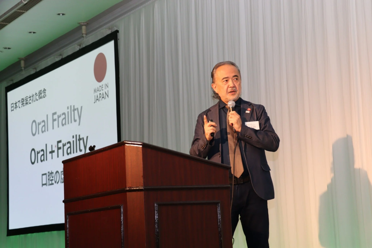 講演中の男性が「Oral Frailty」と表示されたスクリーンを背景に話している