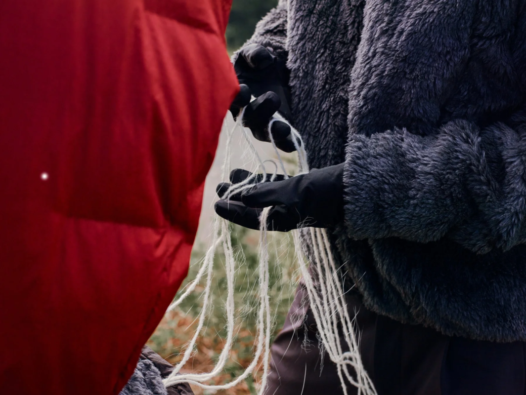 黒い手袋をはめた手が白い糸状のものを操っているクローズアップ