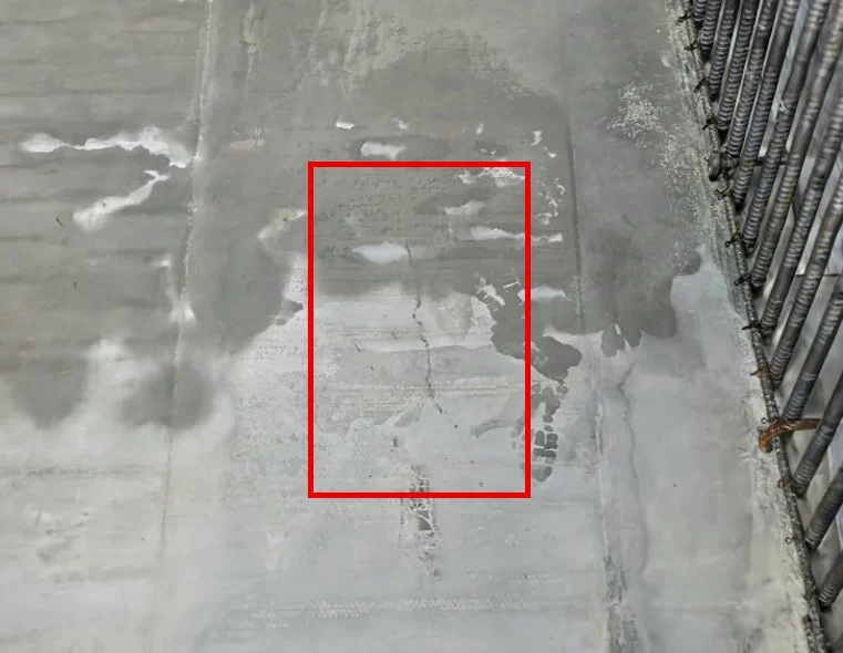 建設現場のコンクリート表面の画像。水濡れ跡やひび割れがあり、右側には鉄筋が見える。赤枠は表面の劣化を示唆