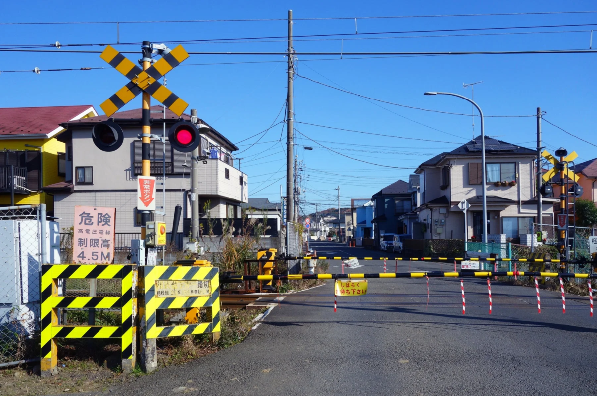 晴れた青空の下、日本の住宅街にある鉄道の踏切が写っています