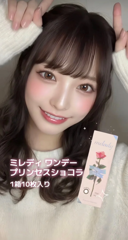 白のニットを着た女性が笑顔で、コンタクトレンズ「ミレディ ワンダー プリンセスショコラ」のパッケージを持っている