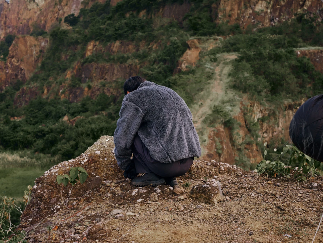 岩だらけの地面にしゃがみこむフリースジャケット姿の人物の後姿