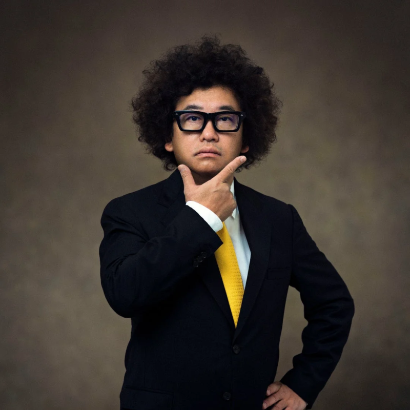 アフロヘアと眼鏡をかけた秋山具義氏のポートレート