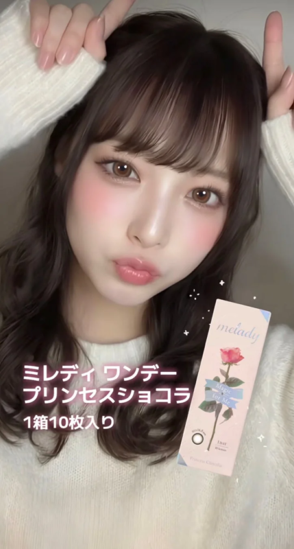 愛らしい表情の女性が、カラコン「ミレディ ワンダー プリンセスショコラ」のパッケージを持ってポーズをとっている