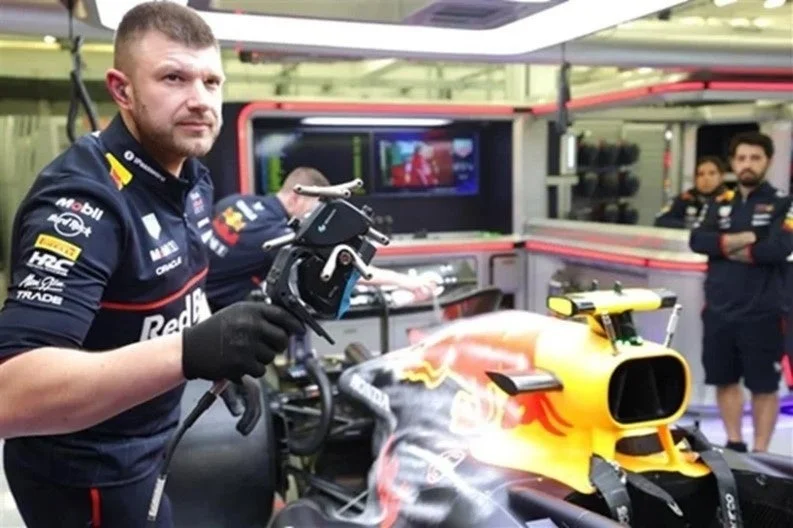 レッドブルレーシングのメカニックがガレージ内でF1マシンを整備している。ツールを手に作業中のメカニックと、背景には他のチームメンバーの姿が見える。