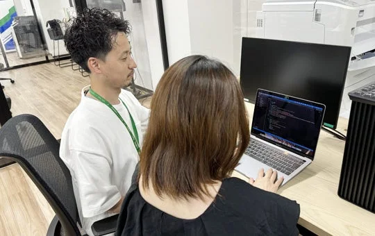 オフィスで男性と女性がノートパソコンを囲んで共同作業をしている様子。